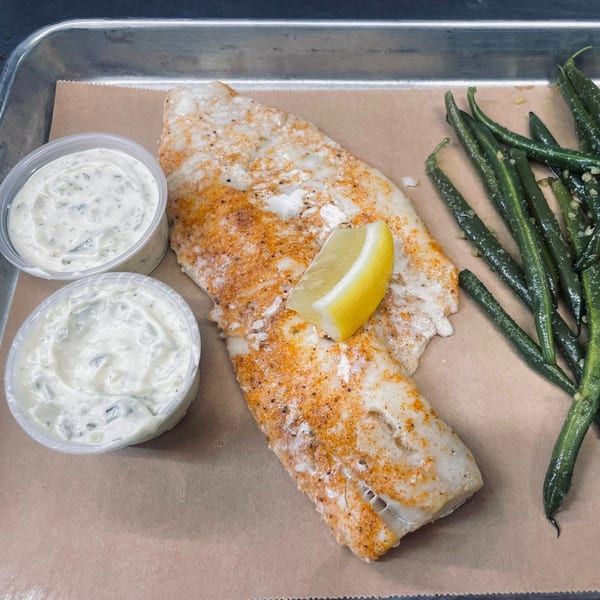 Heintzelman's BBQ Pit's seasoned fish fillet with a lemon wedge, green beans, and two cups of tartar sauce.
