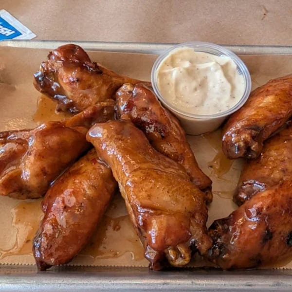 Heintzelman's BBQ Pit's glazed chicken wings with a side of dipping sauce on a metal tray.