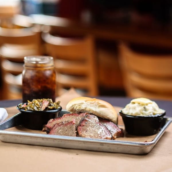 Heintzelman's BBQ Pit brisket plate with sides of collard greens, potato salad, and a drink.