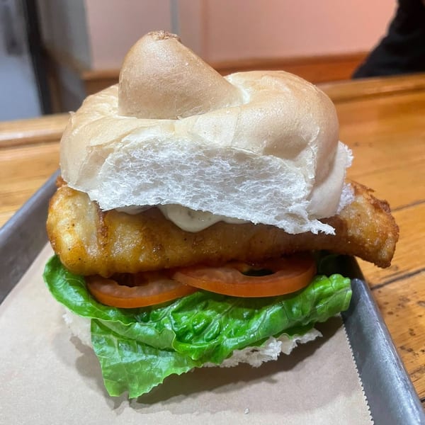 Heintzelman's BBQ Pit fish sandwich with lettuce, tomato, and sauce on a bun.