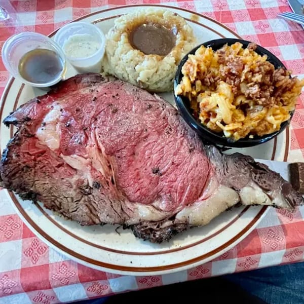 Heintzelman's BBQ Pit prime rib with mashed potatoes, gravy, and crispy fried onions on a checkered tablecloth.